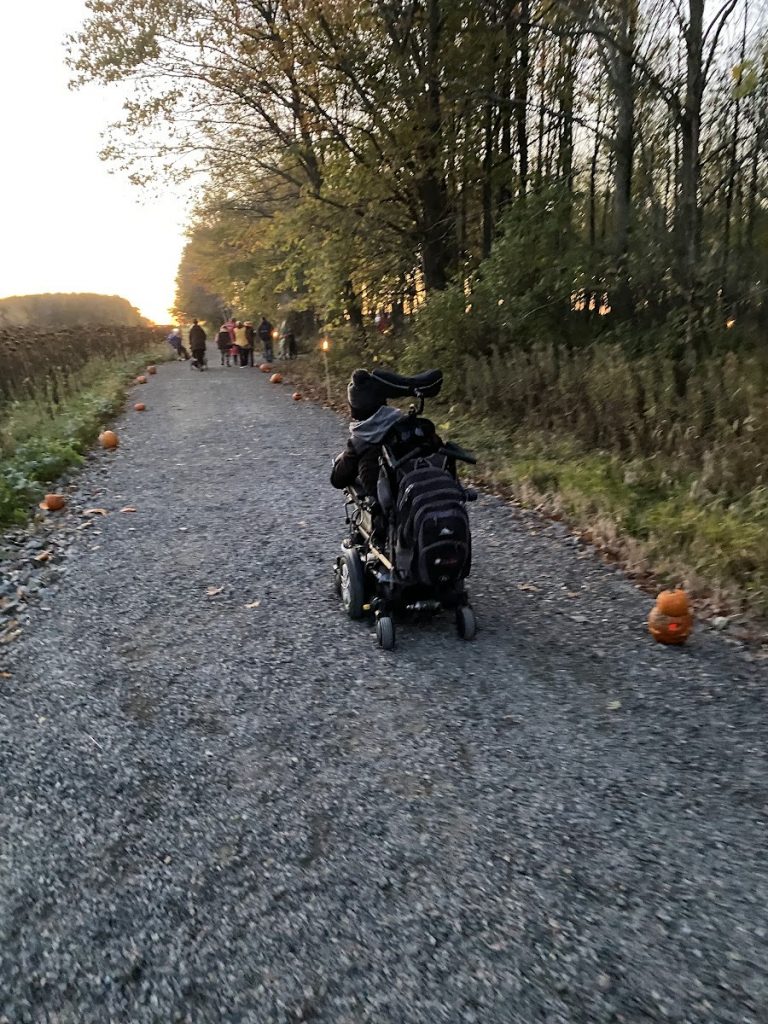 Jordan in his wheelchair, going down a gravel path with jack-o'-lanterns