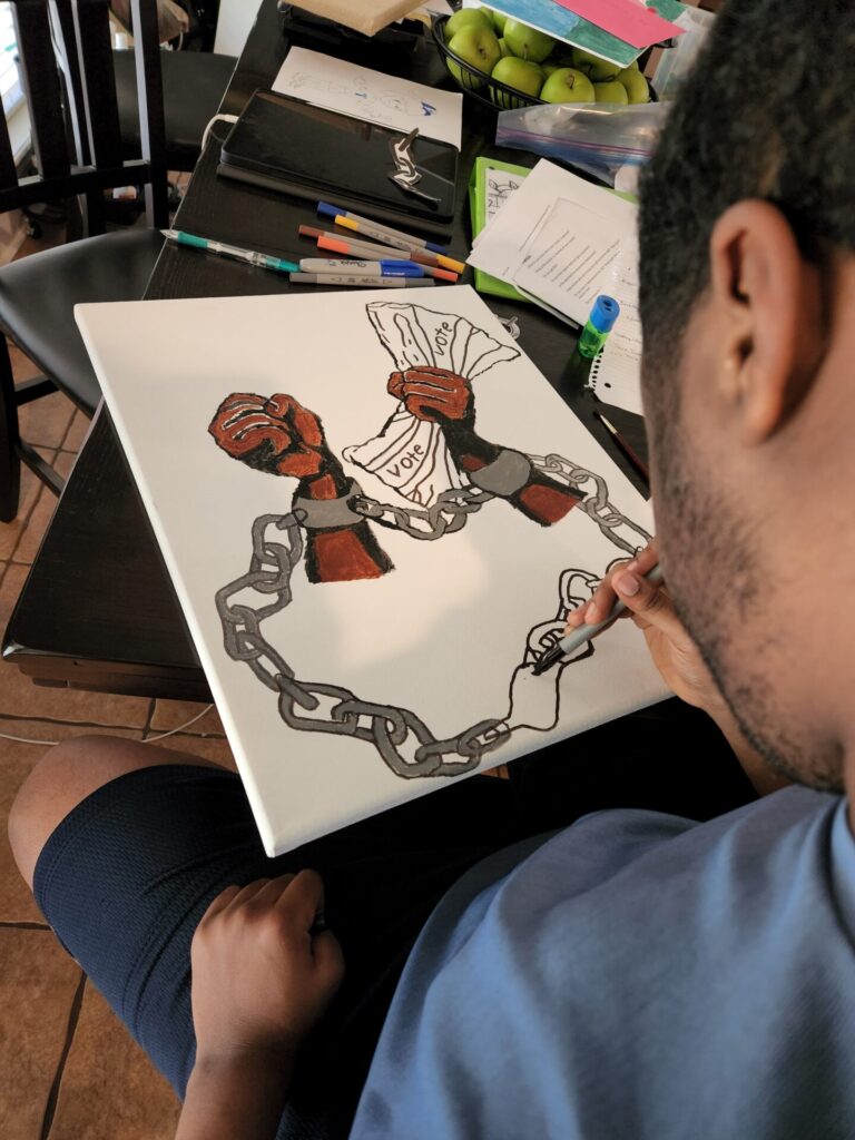 Derek works on a drawing titled "My Vote Suppressed" with two dark-skinned hands closed into fists and in shackles holding Derek's vote