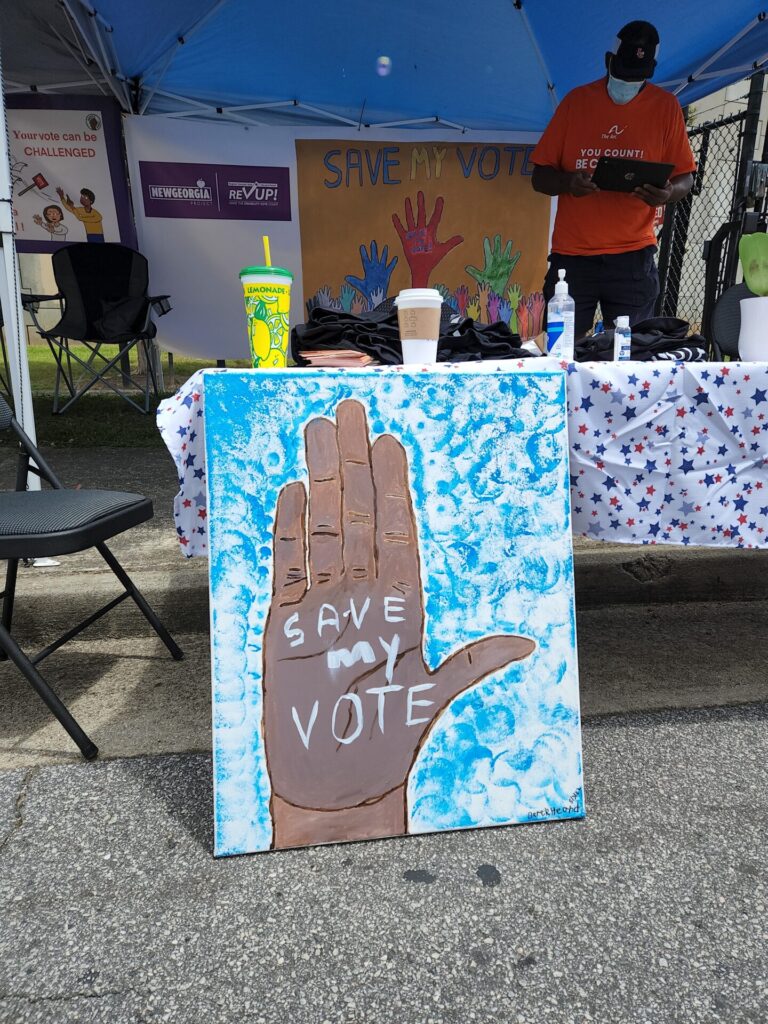 A finished "Save My Vote" painting created by Derek. It shows an open, dark-skinned hand with the text "save my vote" written on the palm